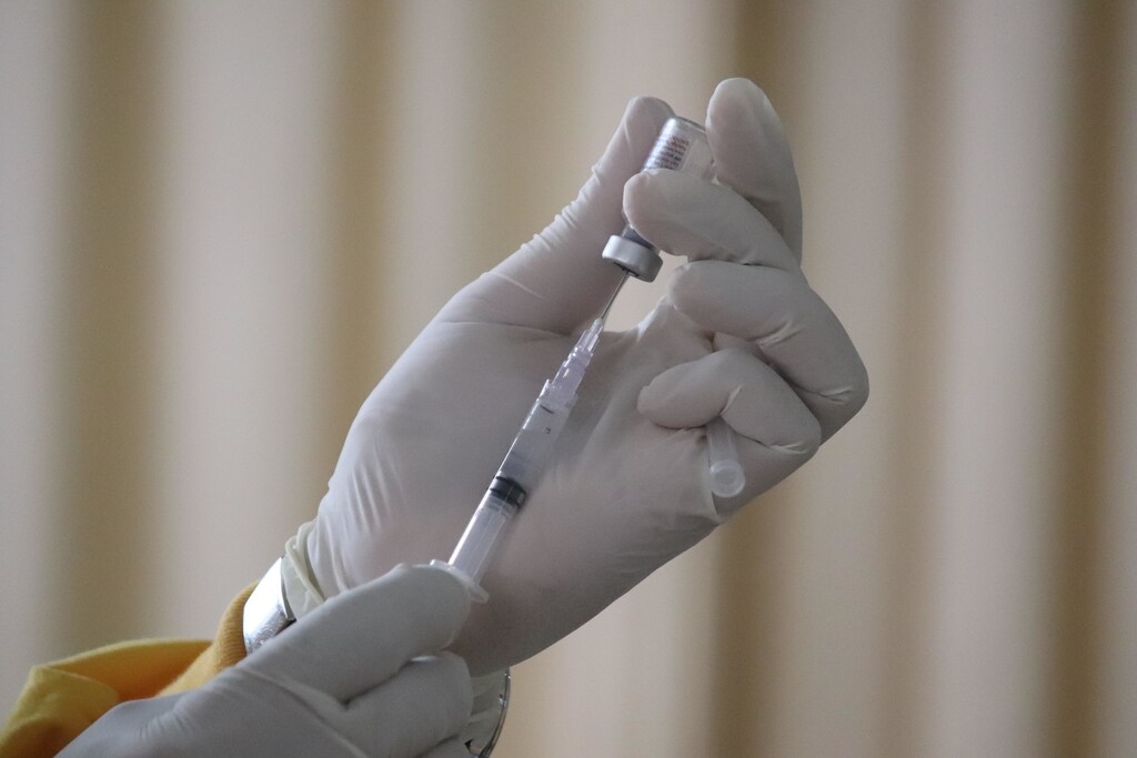 A doctor draws a vaccine dose into a syringe from a bottle
