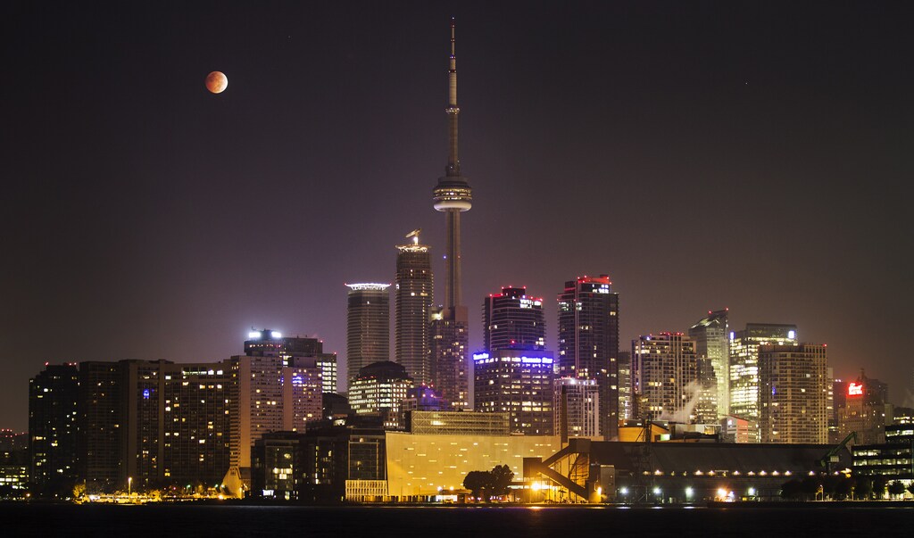 The moon turns orange during a total lunar eclipse behind the CN Tower and the skyline during moonset in Toronto October 8, 2014. The eclipse is also known as a "blood moon" due to the coppery, reddish color the moon takes as it passes into Earth's shadow. The total eclipse is the second of four over a two-year period that began April 15 and concludes on Sept. 28, 2015. The so-called tetrad is unusual because the full eclipses are visible in all or parts of the United States, according to retired NASA astrophysicist Fred Espenak. REUTERS/Mark Blinch (CANADA - Tags: SOCIETY ENVIRONMENT CITYSCAPE TPX IMAGES OF THE DAY) - GM1EAA81KI601