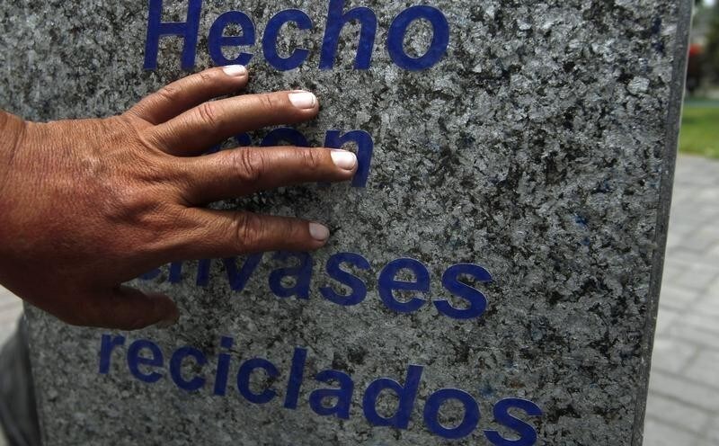 A worker gestures to a poly aluminium plate made of recycled Tetra Pak packages in a park in Lima December 20, 2011. A 8m (26 feet) tall Christmas tree built with 3,500 Tetra Pak carton packages is installed in the park. The tree is promoting the recycling of Tetra Pak packages into poly aluminium plates that are used to make furniture. The sign reads: "Made of recycled Tetra Pack packages".