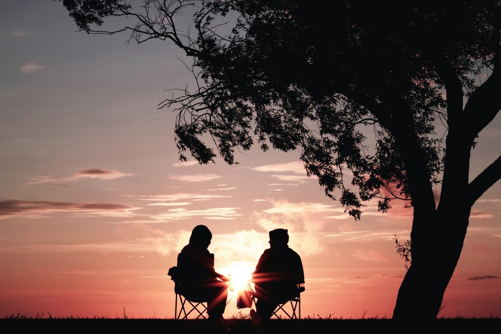 Two people, silhouetted, sitting toward each other, engulfed in meaningful conversations as a pink-hued sun sets behind them