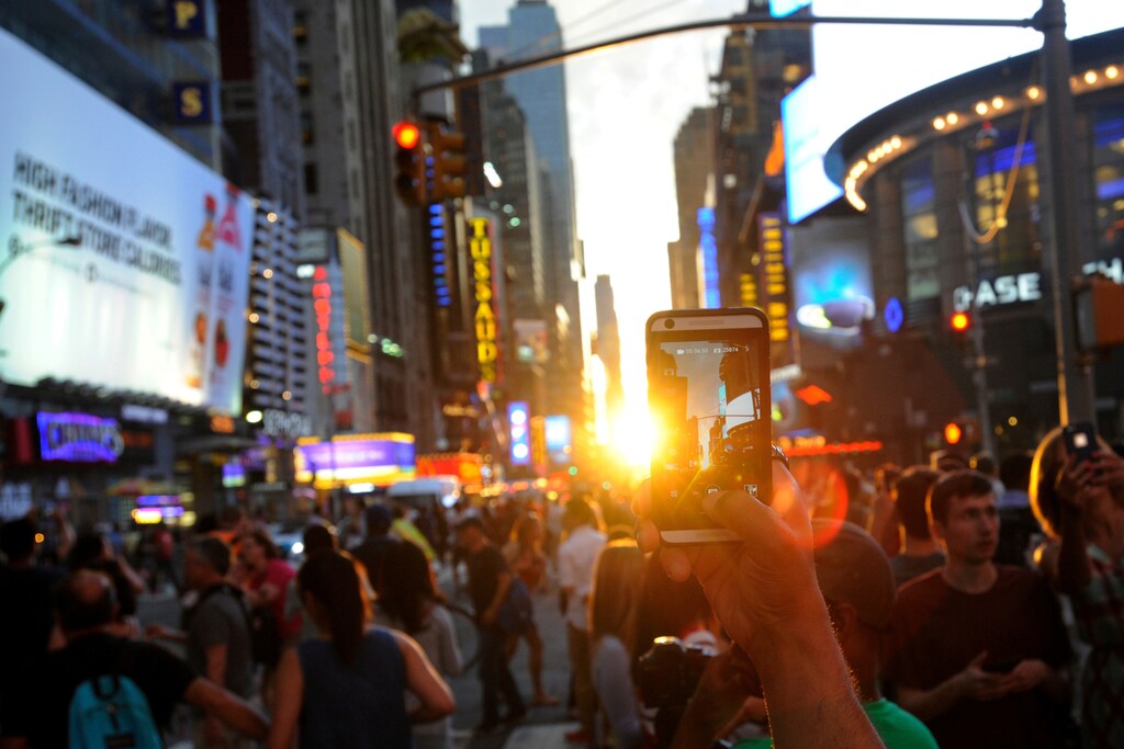 A man takes a photo with her phone as the sun sets over Manhattan aligned exactly with the streets in a phenomenon known as "Manhattanhenge", in New York City, U.S., July 11, 2016. REUTERS/Mark Kauzlarich - RTSHGZ3