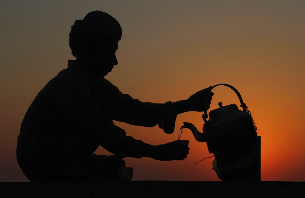 An Afghan man Mir Ali, 22, is silhouetted against the setting sun as he serves green tea to a customer in Karachi December 18, 2011. REUTERS/Athar Hussain (PAKISTAN - Tags: SOCIETY) - GM1E7CI1T9501