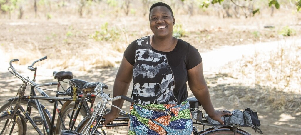 A woman leaning against a bike, smiling at the camera.