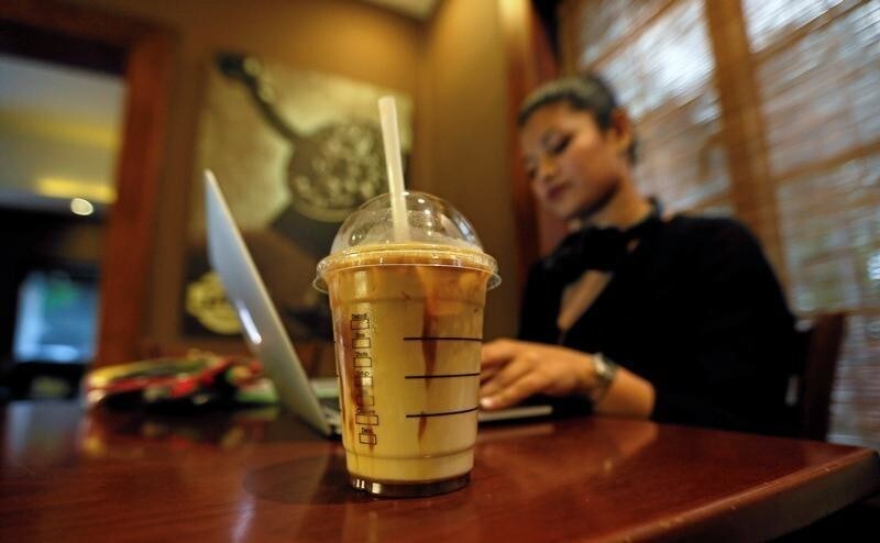 A cup of iced coffee is seen, as a woman works on her laptop, at Java Lounge coffee shop in Colombo, Sri Lanka May 4, 2017. REUTERS/Dinuka Liyanawatte - RC1730CFB120