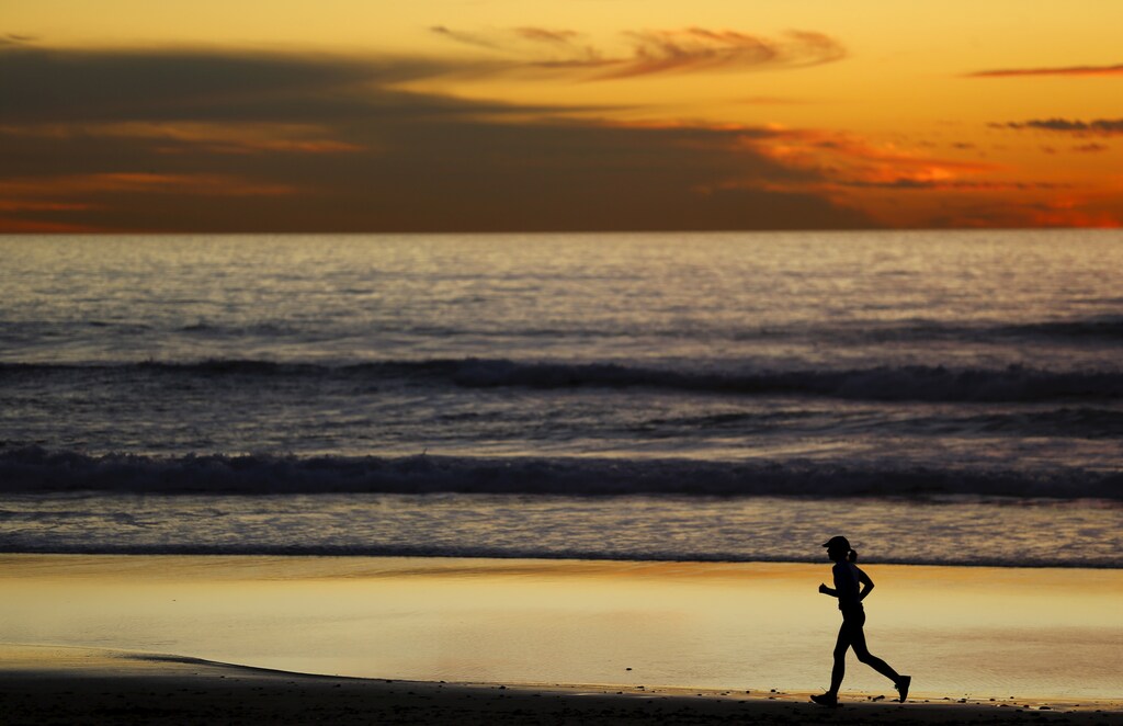 A woman jogs along the beach after sunset in Cardiff, California January 27, 2016. REUTERS/Mike Blake - GF10000287223