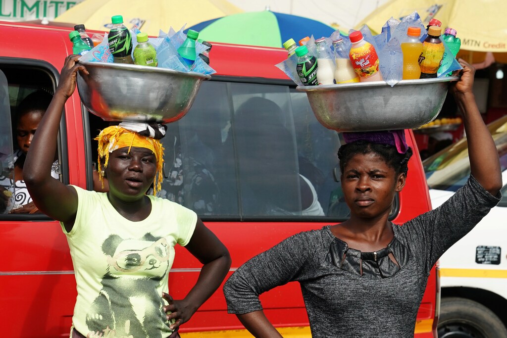 Women carrying drinks on their heads watch as the motorcade that carries the media covering U.S. first lady Melania Trump passes in Accra, Ghana, October 2, 2018. REUTERS/Carlo Allegri - RC16F58BE910