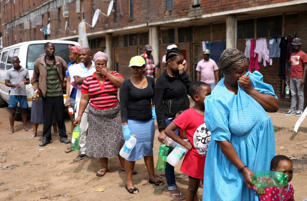 Residents of Madala Men's Hostel cover their noses as they stand in a queue waiting to collect sanitiser from health workers during a nationwide lockdown for 21 days to try to contain the coronavirus disease (COVID-19) outbreak, in Alexandra, South Africa April 1, 2020. REUTERS/Siphiwe Sibeko - RC2QVF9CAZ09