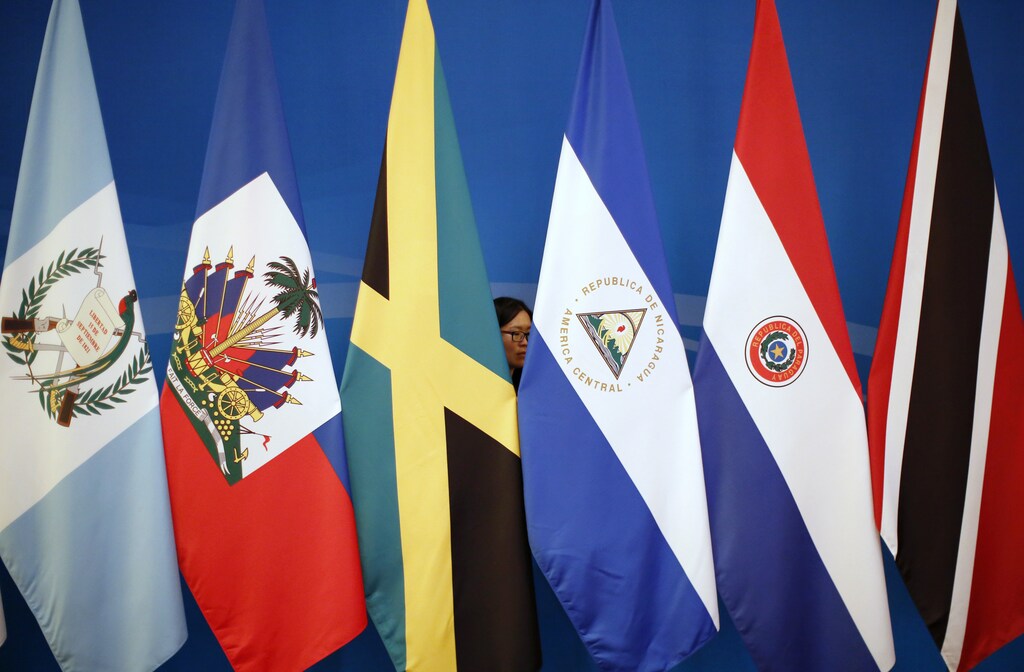 Una mujer detrás de las bandera de países de América Latina mientras las baja luego de la primera reunión Ministerial de China-CELAC