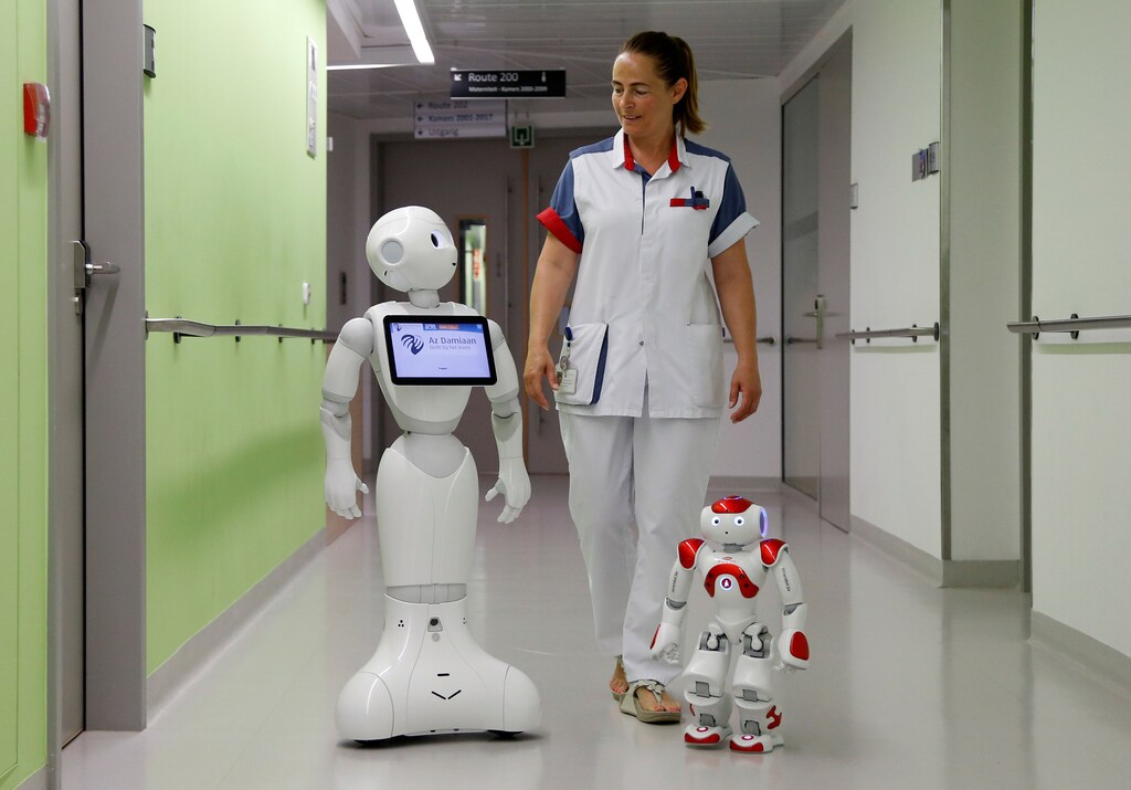 A nurse walks with "Pepper" (L) and "Zora" the robots, humanoid robots designed to welcome and take care of visitors and patients, at AZ Damiaan hospital in Ostend, Belgium June 16, 2016. REUTERS/Francois Lenoir - D1AETKGAYXAA