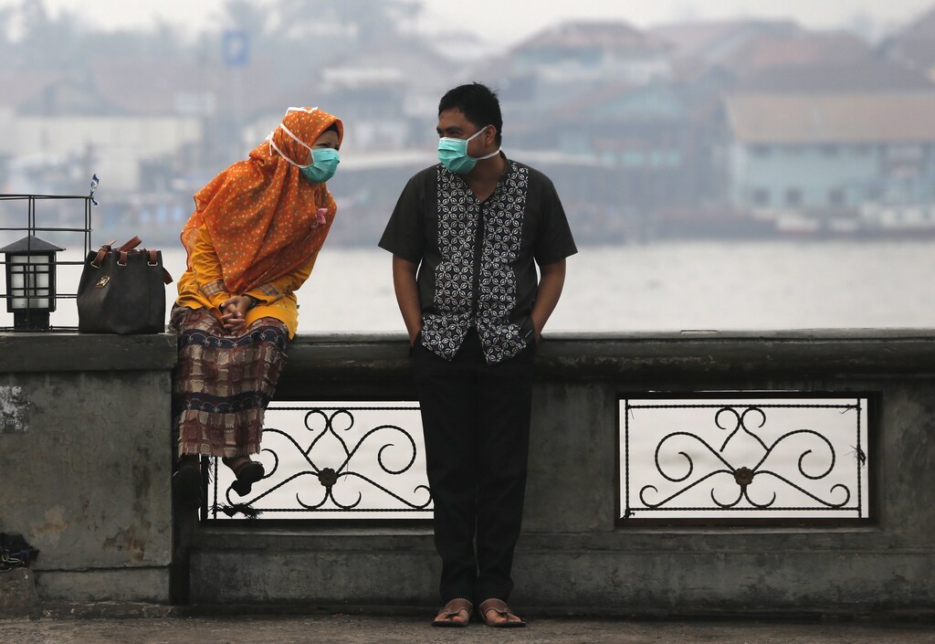 A couple, wearing face masks to protect themselves from the haze, talk near Musi River in Palembang, on the Indonesian island of Sumatra, September 20, 2015. Indonesia will take 30 days to bring smouldering forest fires under control, the national disaster management agency said on Friday, as smog from the fires pushes pollution in Southeast Asia to record highs. REUTERS/Beawiharta - RTS1XXB