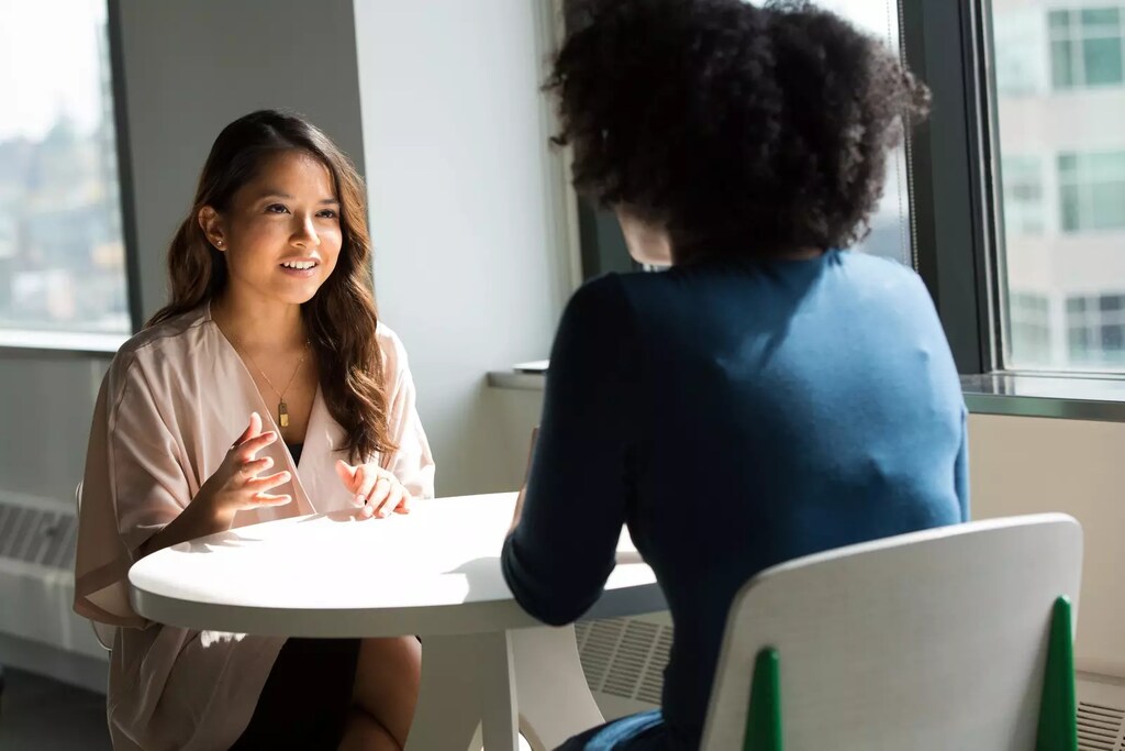 Esta imagen muestra a dos personas hablando a través de una mesa, ilustrando una escucha generosa.