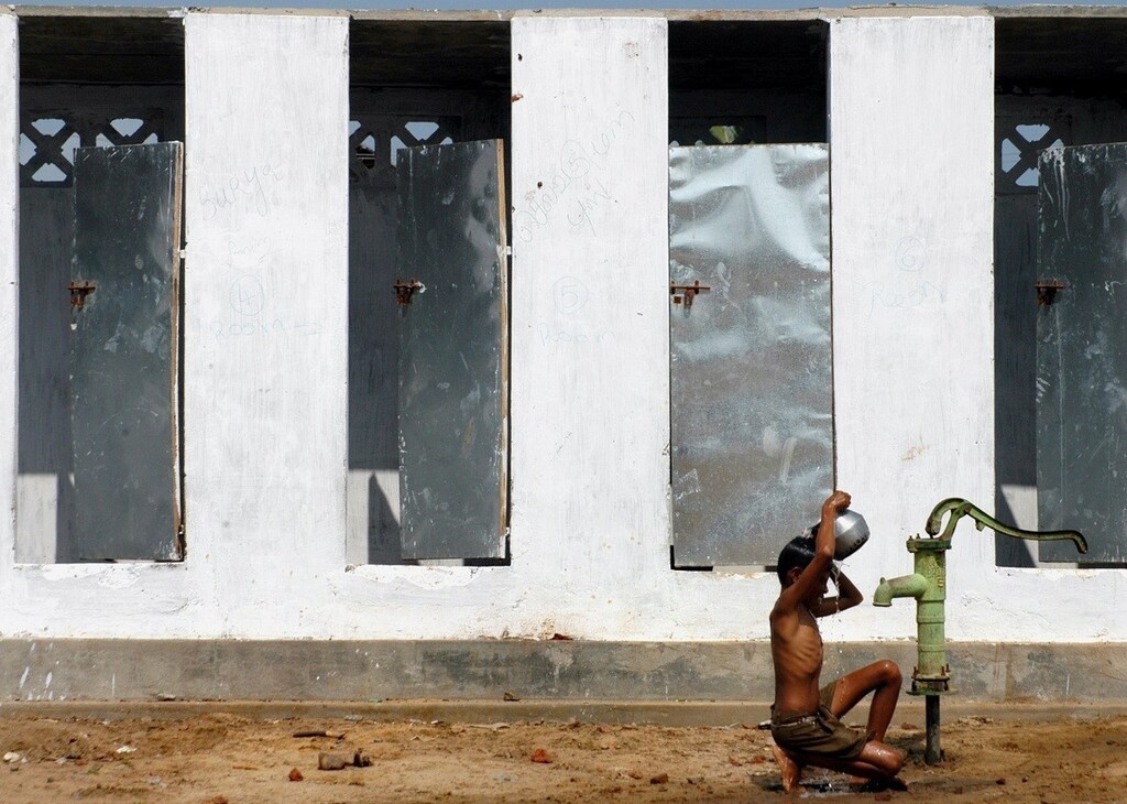 A boy takes bath outside newly built toilets in a village on the outskirts of Nagapattinam, about 325km (202 miles) from the southern Indian city of Chennai December 24, 2005. Government and multilateral agencies have pledged more than $7.3 billion in aid for nations hit by the December 26, 2004 earthquake and tsunami in the Indian Ocean, while global private donations amount to more than $5.7 billion. REUTERS/Jagadeesh NV - RTR1BITH
