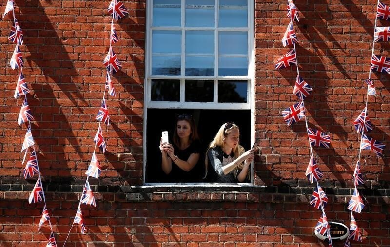 Women take photos on their smartphones as they lean out of the window of a building near Windsor Castle in Windsor, Britain, May 17, 2018. REUTERS/Damir Sagolj - RC1AD97D46F0