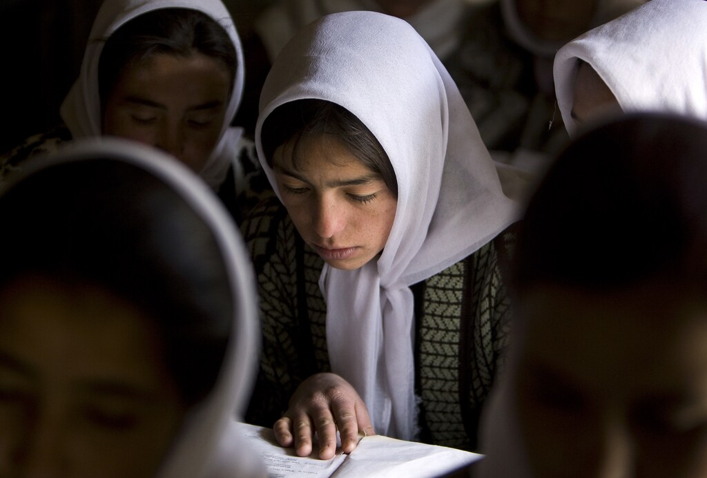 An Afghan girl reads a book in a classroom among other female students