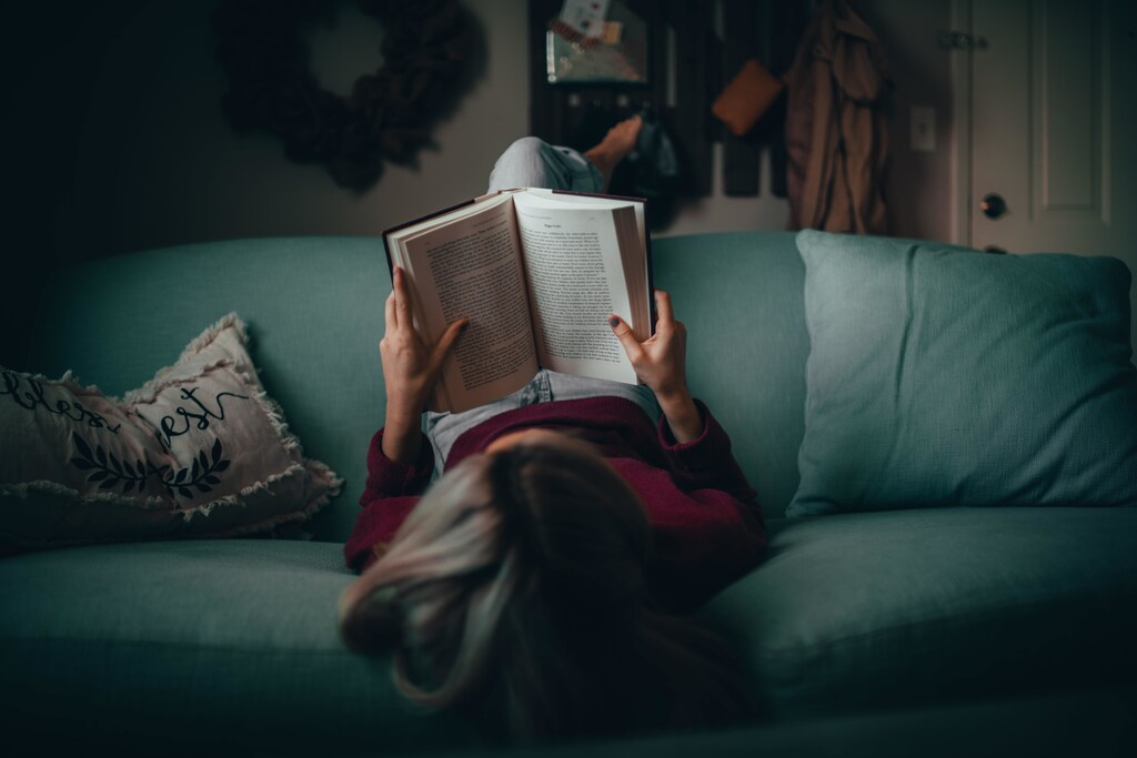 A person laying on the sofa. reading a book.