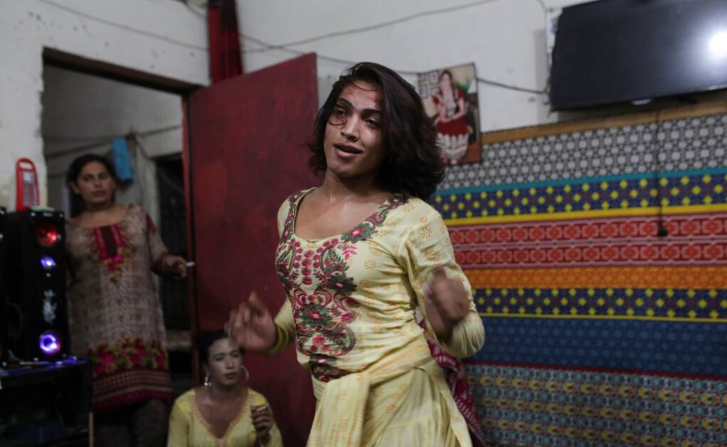 A transgender woman dances in a dimly lit room, as two other women watch her from behind in Lahore, Pakistan.