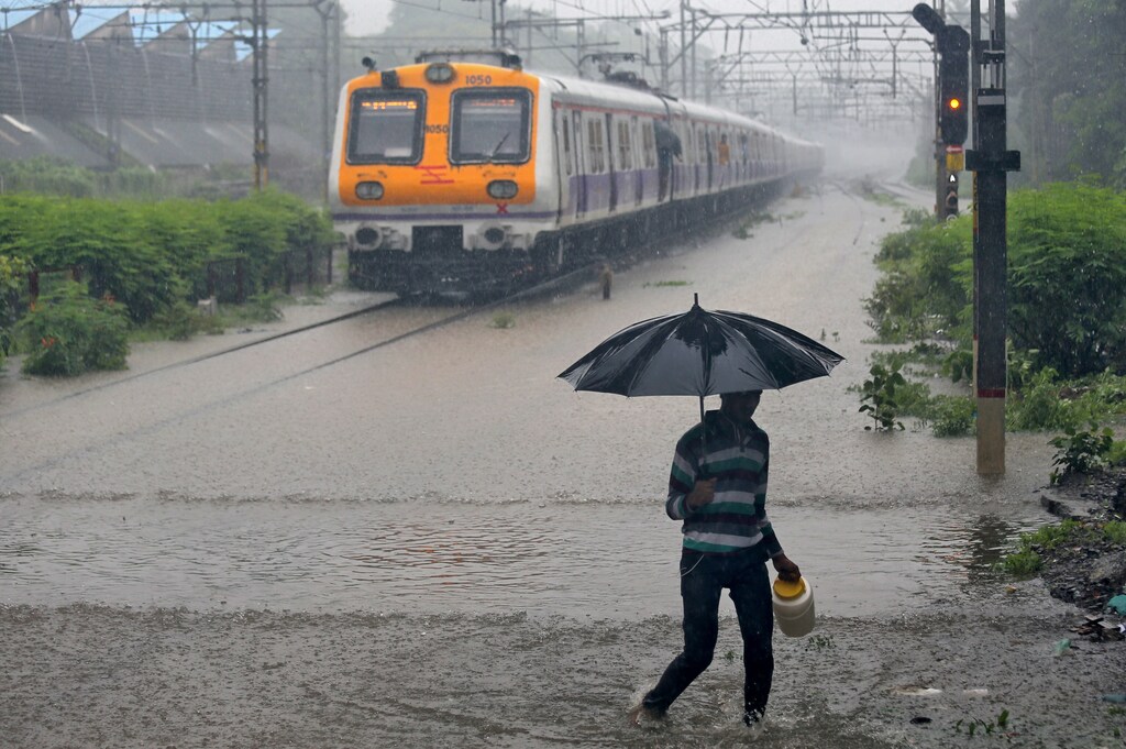 A man carrying an umbrella walks past a passenger train that moves through a water-logged track during heavy rains in Mumbai, India, July 9, 2018. REUTERS/Francis Mascarenhas