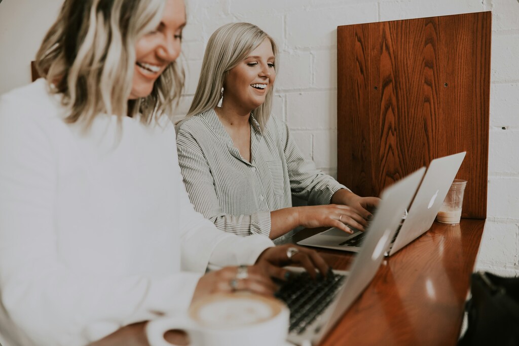 Dos mujeres ríen mientras utilizan laptops.