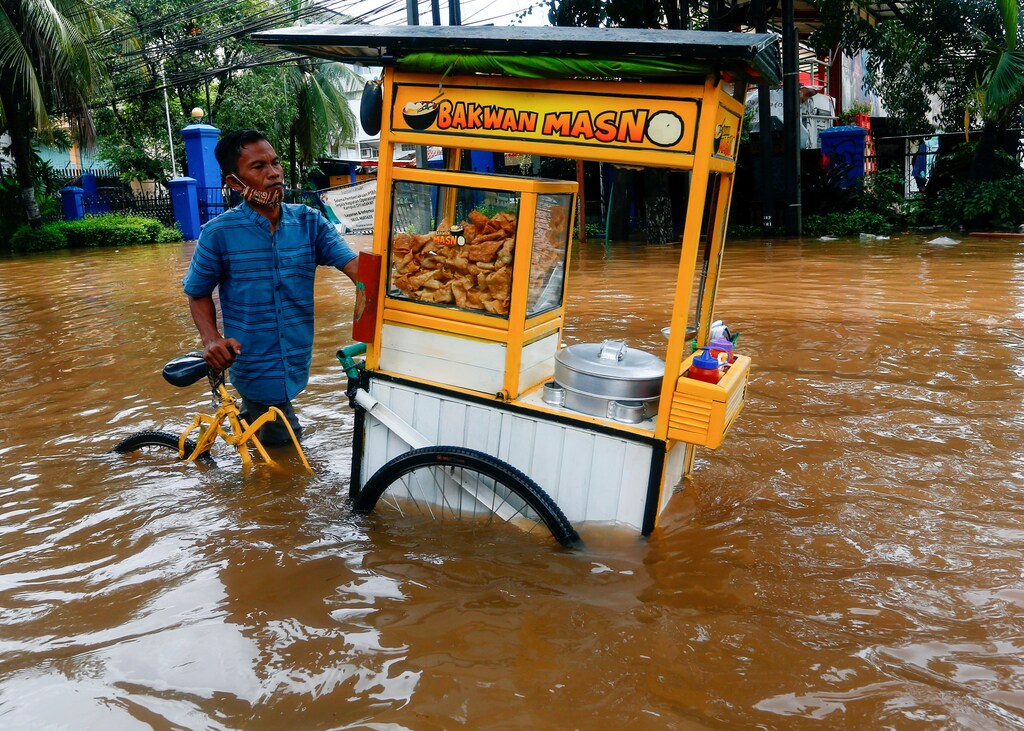 A street vendor pushes his cart through the water in an area affected by floods following heavy rains in Jakarta, Indonesia, February 20, 2021. REUTERS/Ajeng Dinar Ulfiana TPX IMAGES OF THE DAY - RC27WL9PY0L8
