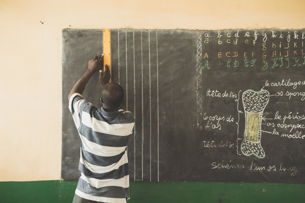 A man in a black and white shirt writing on a chalk board