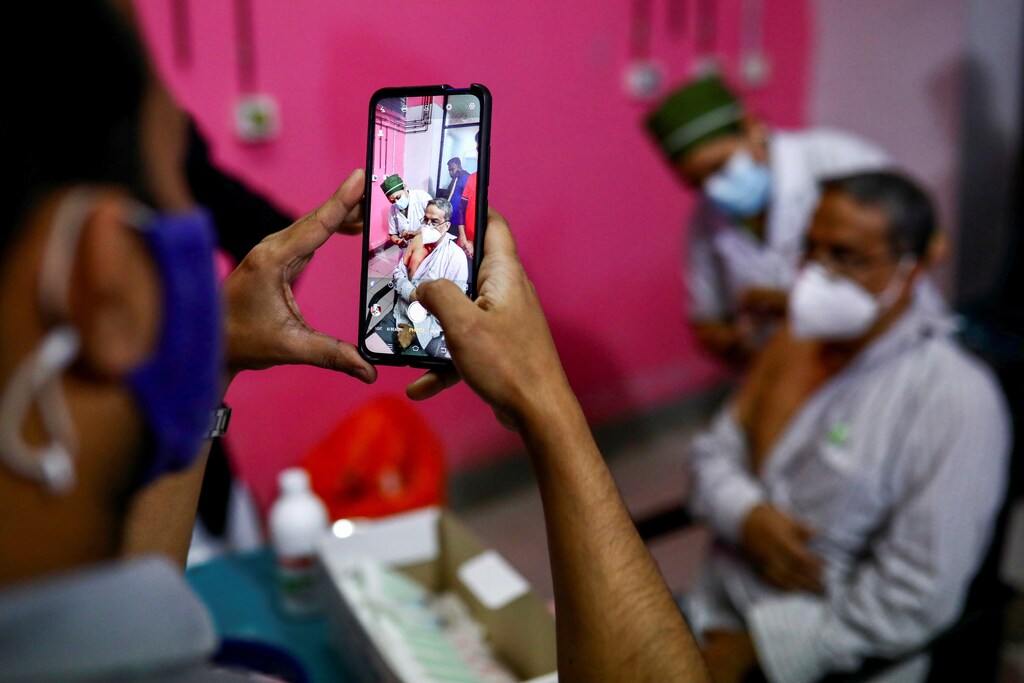 A man takes picture while a nurse injects the Oxford-AstraZeneca's Covishield vaccine to a man at the Dhaka Medical College vaccination centre in Dhaka, Bangladesh, February 9, 2021. REUTERS - RC2WOL9CFUL8