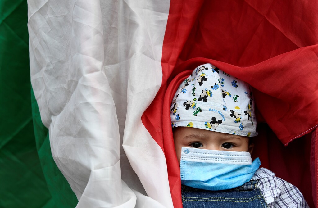 A child wearing a protective face mask is seen next to Italian flag during a protest in front of the town hall, as Italy eases some of the lockdown measures put in place during the coronavirus disease (COVID-19) outbreak, in Milan, Italy May 18, 2020. REUTERS/Flavio Lo Scalzo TPX IMAGES OF THE DAY - RC2WQG9E3CZZ