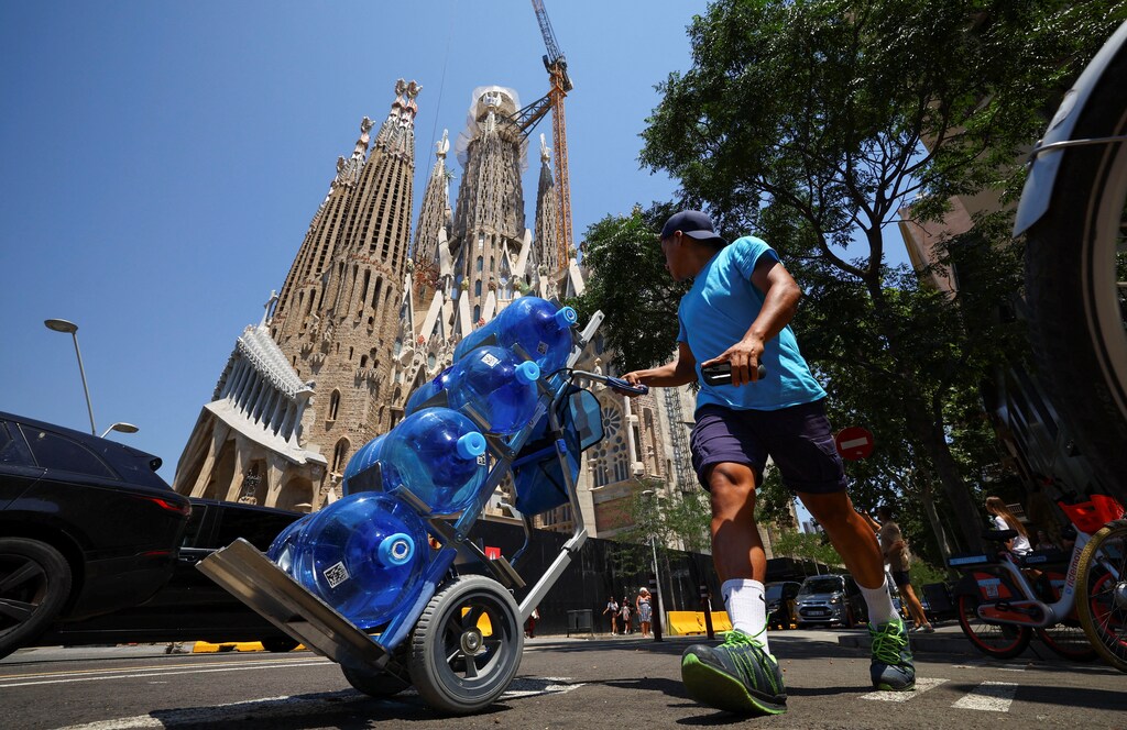 A delivery man carries water as he walks past the Sagrada Familia Basilica during a heatwave in Barcelona, Spain June 30, 2025. REUTERS/ Albert Gea
