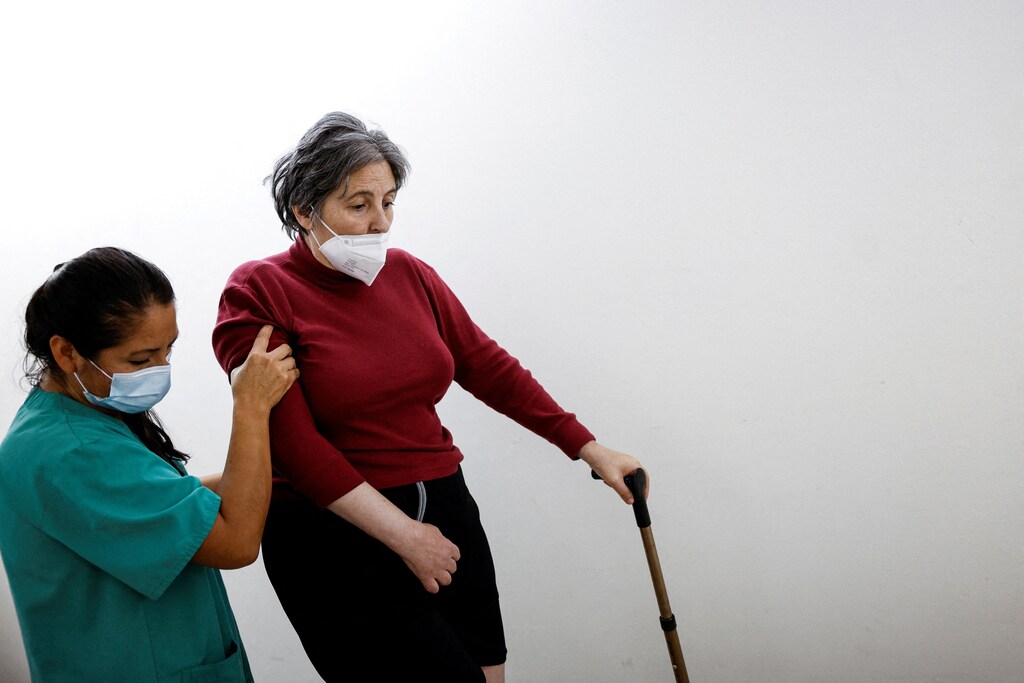 Una superviviente de derrame cerebral camina con un bastón y la ayuda de una fisioterapeuta neurológica en España.