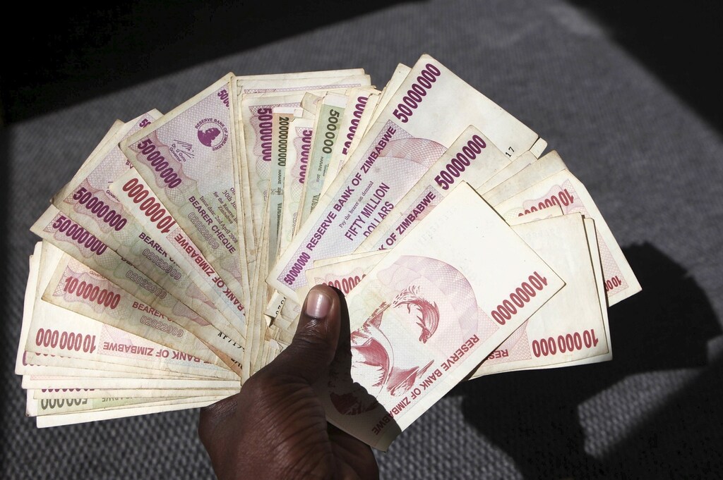 A man poses with a handful of Zimbabwean dollars at a bank in central Harare, June 15, 2015. Zimbabweans began exchanging old notes of local dollars for U.S. dollars, as President Robert Mugabe's government seeks to officially bury the worthless currency. REUTERS/Philimon Bulawayo - RTX1GLMK