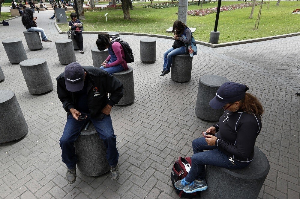 People use their smart phones as they sit at Kennedy park in Miraflores district in Lima.