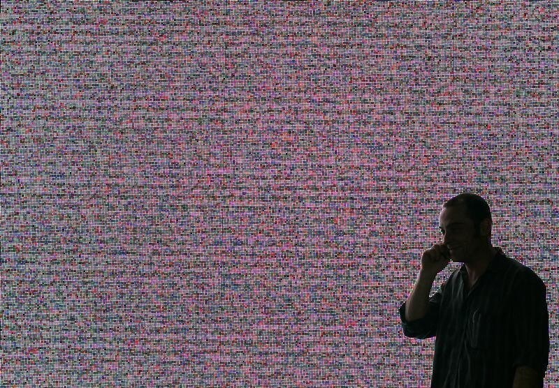 A man uses his mobile phone while standing in front of a large screen in preparation for the CeBIT computer fair in the northern German town of Hanover March 13, 2007. The world's largest computer and information technology fair CeBIT runs from March 15 to March 21, 2007. REUTERS/Hannibal Hanschke (GERMANY) - BM2DUUQNOGAA