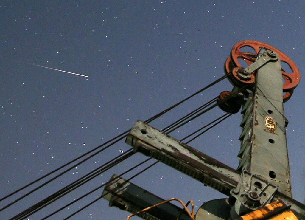 A meteor streaks past stars in the night sky above an excavator at an abandoned coal mine in the village Moscanica, Bosnia and Herzegovina, August 12, 2017. REUTERS/Dado Ruvic - RC14323EED00