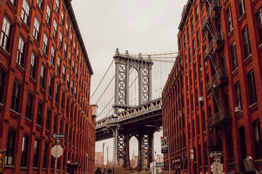 A snap of Brooklyn Bridge between two red brick buildings: Sustainable travel means managing overcrowding at popular tourist and Instagrammable spots.