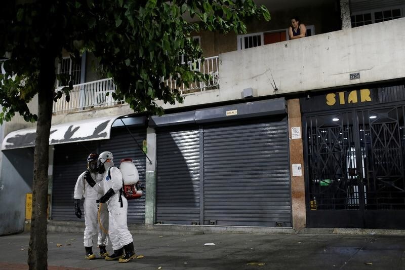 Workers wearing protective suits spray disinfectant solution in the street as a woman watches from her balcony during the national quarantine in response to the spread of coronavirus disease (COVID-19) in Caracas, Venezuela March 22, 2020. REUTERS/Manaure Quintero - RC2FPF9DOZMA