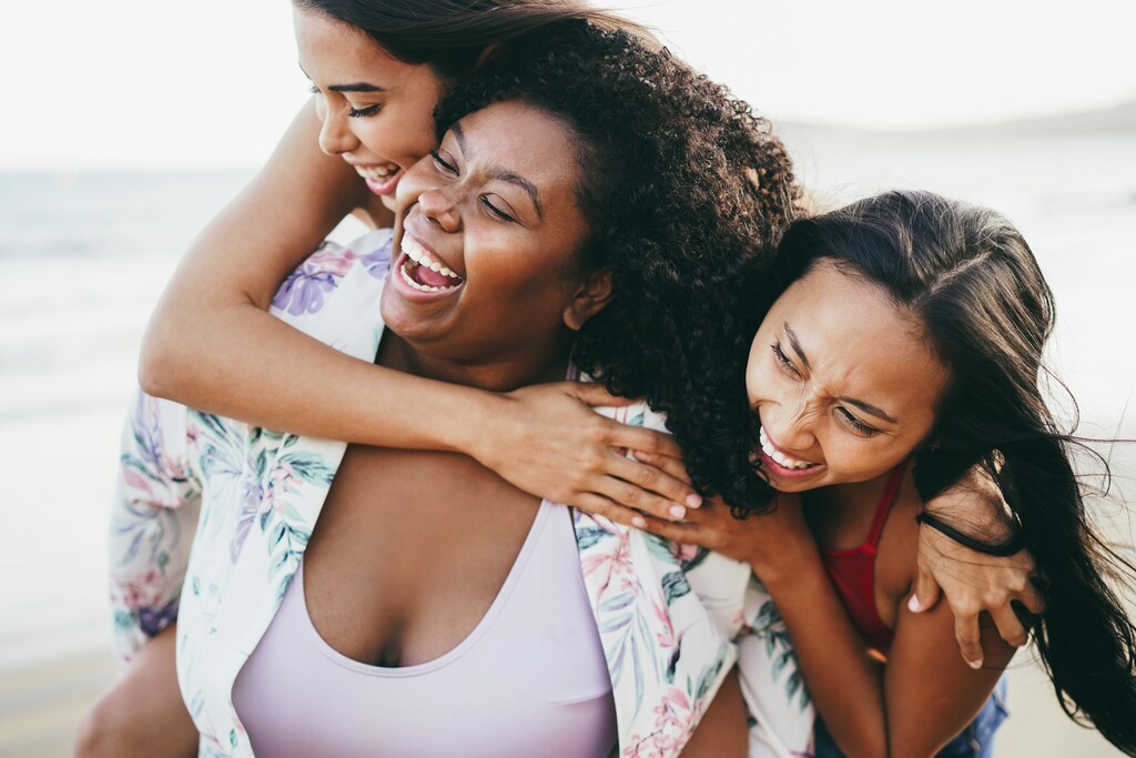 three black women hugging and laughing. Obesity is misunderstood