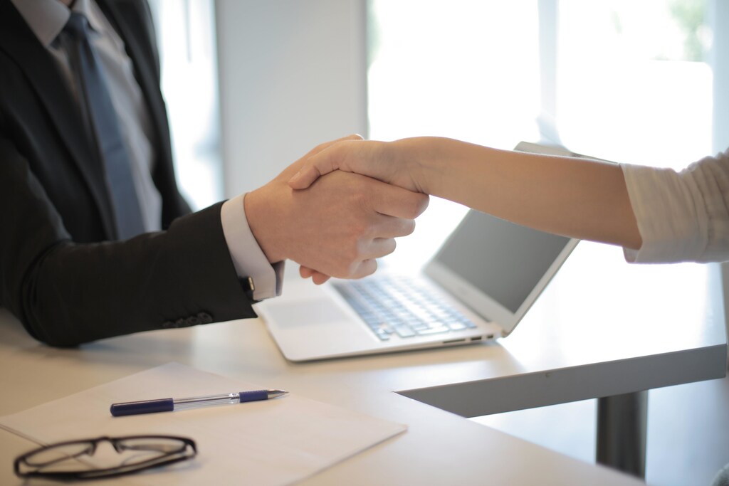 Two workers shaking hands in the workplace with a computer in the background.