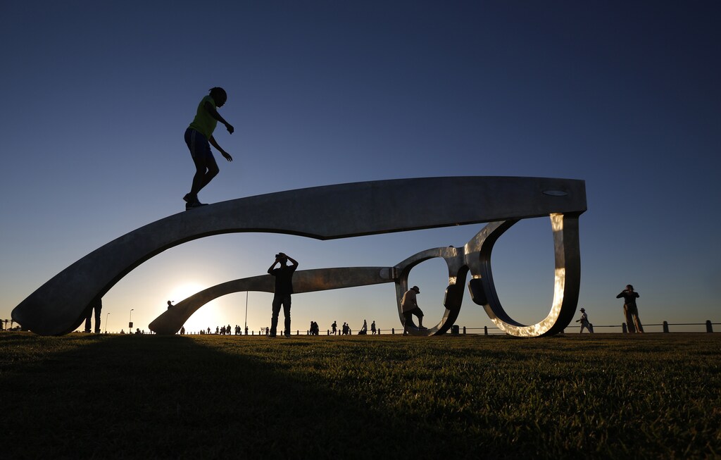 Youths pose for photographs as they climb on top of a sculpture in the form of a giant pair of spectacles on Cape Town's Sea Point Promenade, November 18, 2014. Inspired by Nelson Mandela, the work 'Perceiving Freedom' by artist Michael Elion has stirred some controversy in the local media. While popular with visitors to the promenade, some critics have questioned the association of Mandela's legacy with commercial sponsors. REUTERS/Mike Hutchings (SOUTH AFRICA - Tags: SOCIETY TPX IMAGES OF THE DAY) - GM1EABJ0FR001