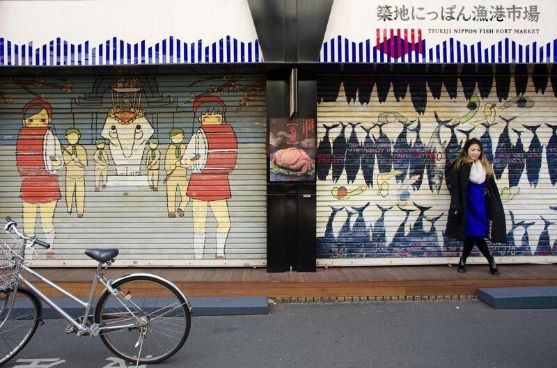 A woman stands in front of a closed shop in the outer part of the Tsukiji fish market, the Jogai Shijo, in Tokyo January 4, 2015. The famous Tsukiji wholesale fish and seafood market, is scheduled to leave its fabled 80-year-old halls to move into bigger, more modern facilities next year ahead of the 2020 Tokyo Olympics. The outer part of the market, the Jogai Shijo, that caters to the public will stay in its old place, but critics wonder about its chances for survival without the world's biggest fish trading place at its doorsteps. Picture taken January 4, 2015. REUTERS/Thomas Peter (JAPAN - Tags: BUSINESS SOCIETY) - GM1EB161DA001