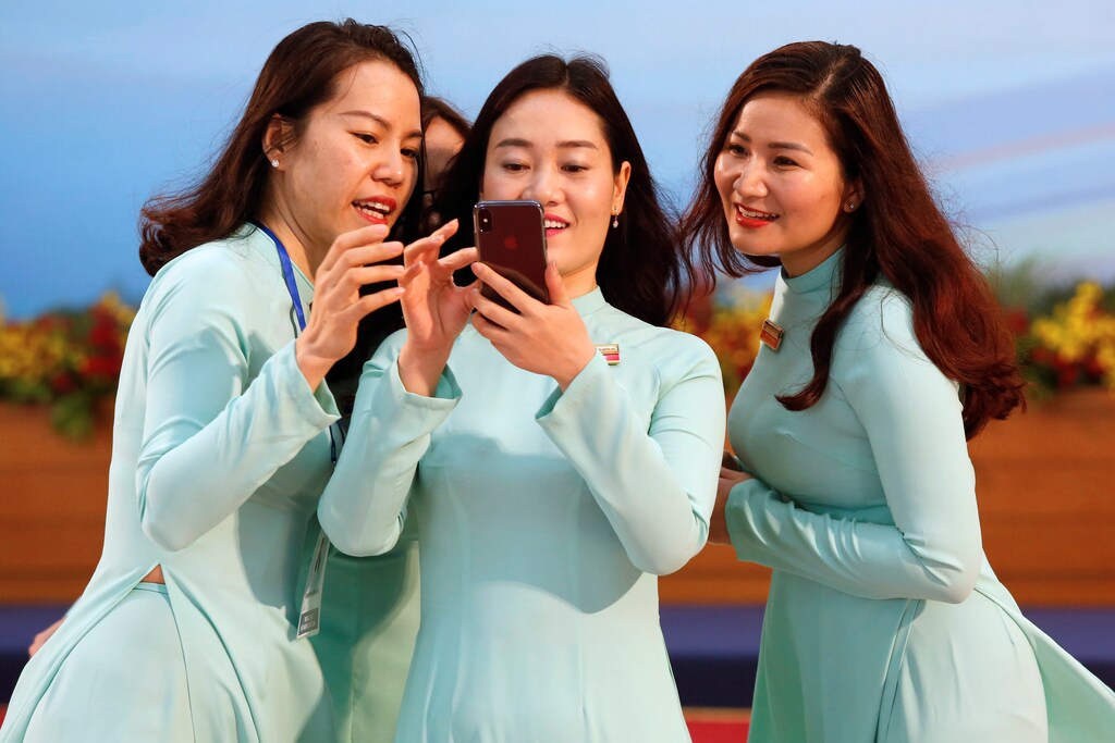 Vietnamese women wearing the traditional 'dao dai' long dress take a selfie at the National Convention Centre in Ha Noi, Viet Nam, March 2018.