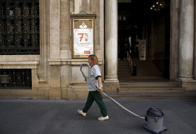 A cleaner pulls a vacuum cleaner as she walks past a Santander Bank branch in the Andalusian capital of Seville, southern Spain September 16, 2013.
