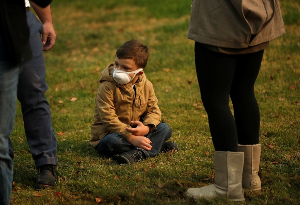 A child wears a mask to protect them from smoke as they watch the motorcade of U.S. President Donald Trump pass by on its way to the operations center near Paradise in Chico, California, U.S., November 17, 2018. REUTERS/ Leah Millis - RC15C05AE9E0