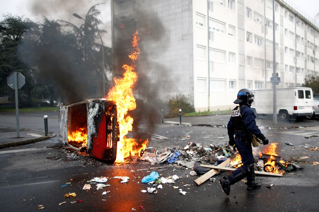 A French riot policeman walks past a burning car as youth and high school students protest against the French government's reform plan, in Nantes, France, December 6, 2018. REUTERS/Stephane Mahe - RC1D67250D70