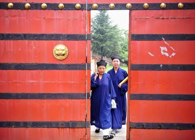 A female Taoist priest (L) talks on her mobile phone as she walks with a fellow priest towards a wooden door at Yuquan Yuan (Jade Spring Taoist Temple) at the foot of Mount Hua, in Huayin, Shaanxi province July 4, 2012. More than 60 priests from all over China gathered at this temple for a two-month course of Taoist music, which is an essential element to many Taoist ceremonies, local media reported. Picture taken July 4, 2012.