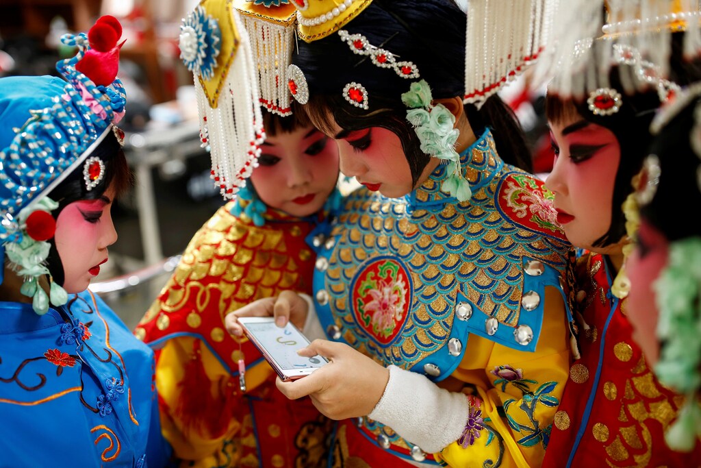 A participant plays a game on her phone as others watch during a break in a traditional Chinese opera competition at the National Academy of Chinese Theatre Arts in Beijing, China, November 26, 2016. REUTERS/Thomas Peter TPX IMAGES OF THE DAY - RC134BA8F8F0