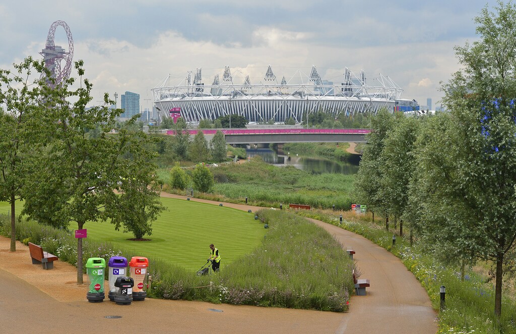 A worker mows grass, with the Olympic Stadium seen in the background, at the Olympic Park in Stratford, the location of the London 2012 Olympic Games, in east London July 20, 2012. REUTERS/Toby Melville (BRITAIN - Tags: SPORT OLYMPICS) - GM1E87K1KRJ01