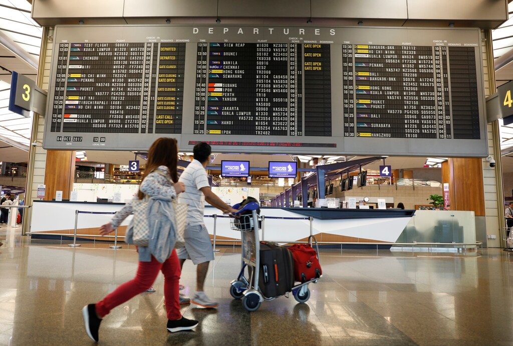 People pass a departures flight information board at Changi Airport's Terminal Two in Singapore October 4, 2017. REUTERS/Edgar Su - RC1F6585D200