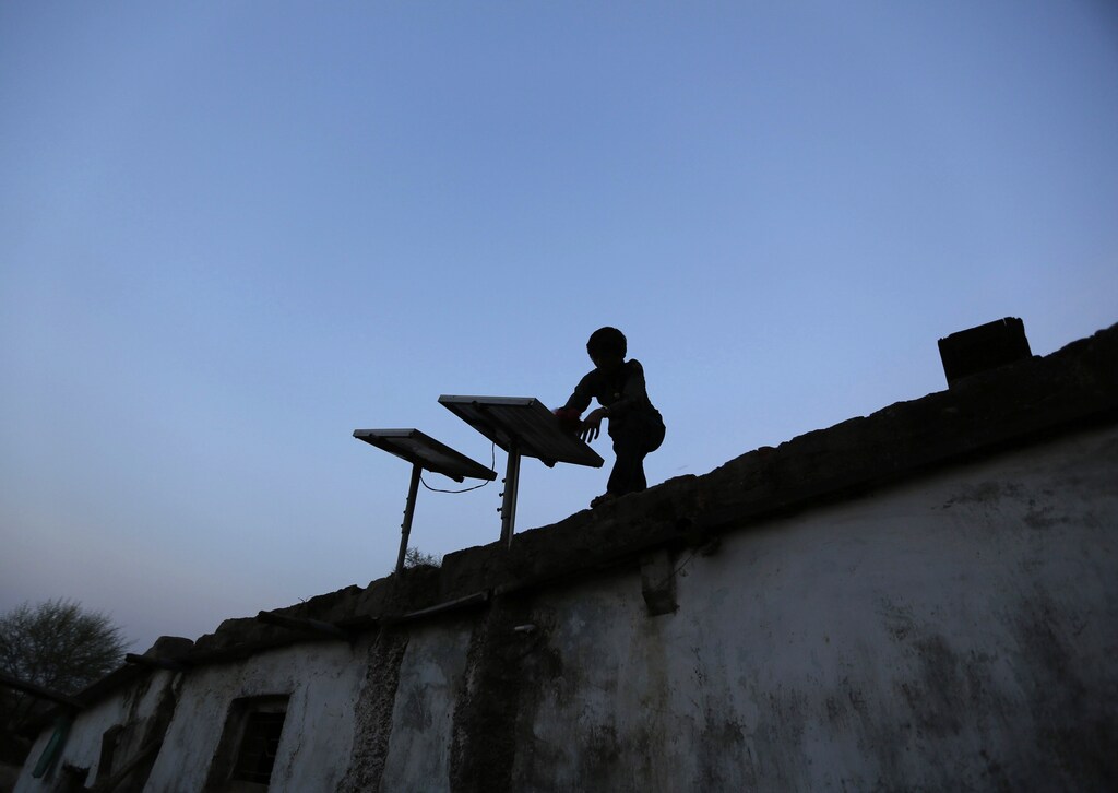 A boy dusts off a solar panel installed on the rooftop of his house on the outskirts of the western Indian city of Ahmedabad October 27, 2014.