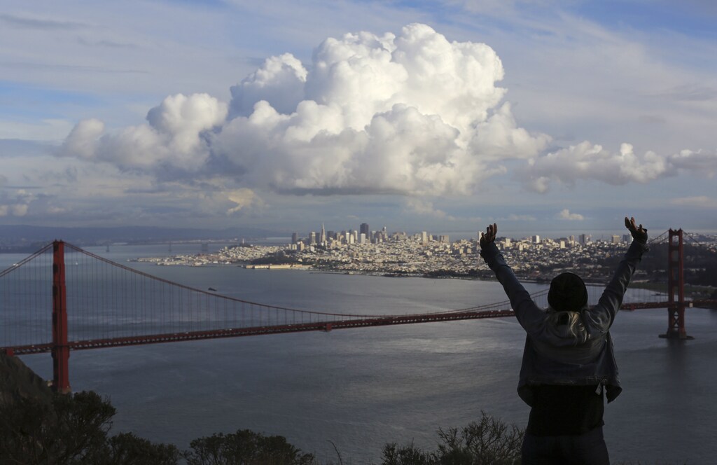 A visitor to the Marin Headlands reacts while looking out over the Golden Gate Bridge and skyline of San Francisco, as a large cloud gathers over the city, December 12, 2014. A major storm pummeled California and the Pacific Northwest with heavy rain and high winds on Thursday, killing one man, knocking out power to tens of thousands of homes, disrupting flights and prompting schools to close. REUTERS/Robert Galbraith