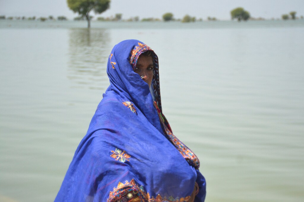 A woman, displaced because of the floods, walks with her belongings covered with scarf, with the flood water in the background, following rains and floods during the monsoon season in Sehwan, Pakistan September 20, 2022.