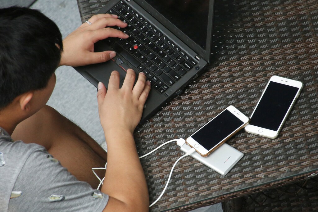 Two mobile phones lie on a table as a man uses a laptop at a cafe in Beijing, China June 3, 2017. REUTERS/Thomas Peter - RC1A9502B9A0
